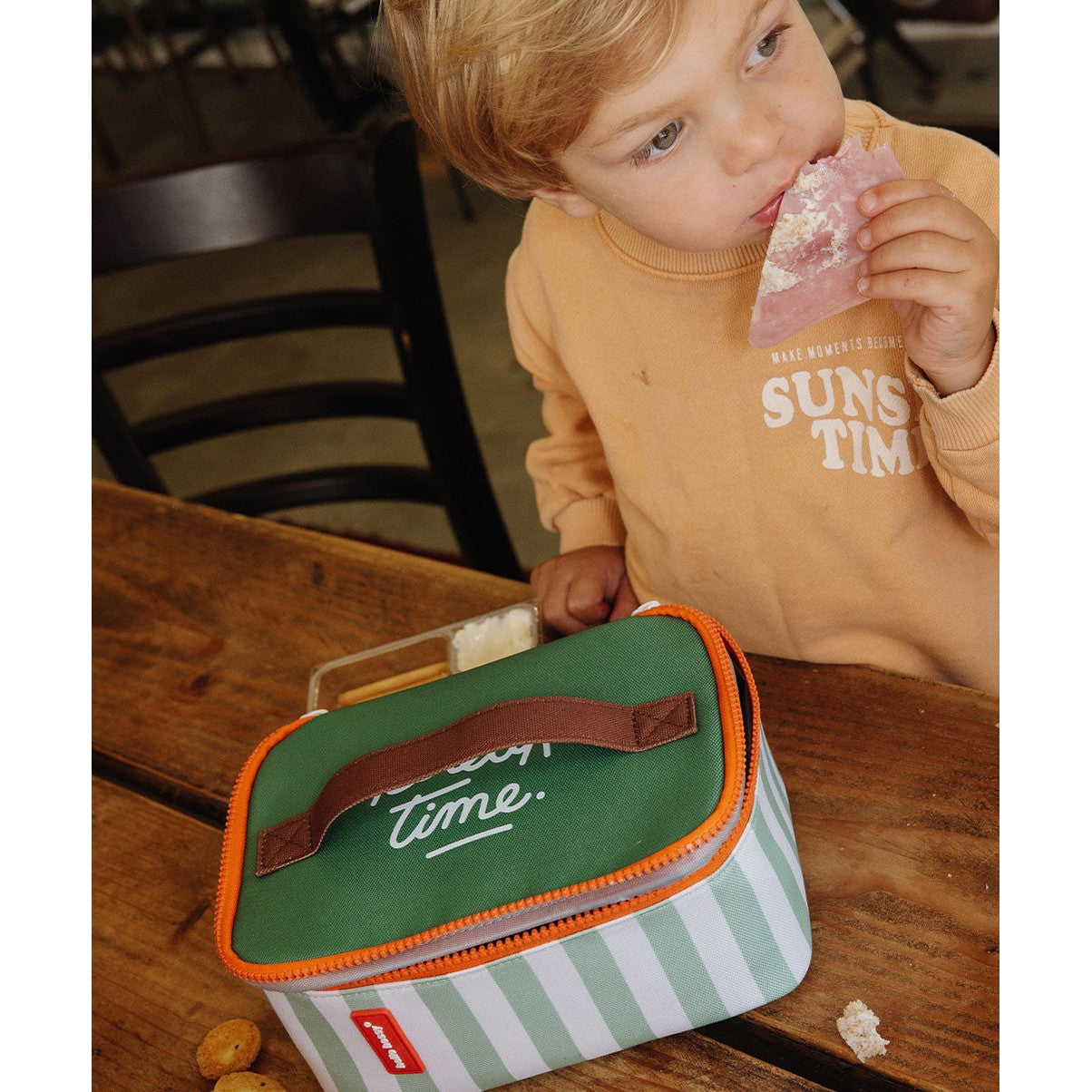 Boy eating at table with closed green striped lunch bag