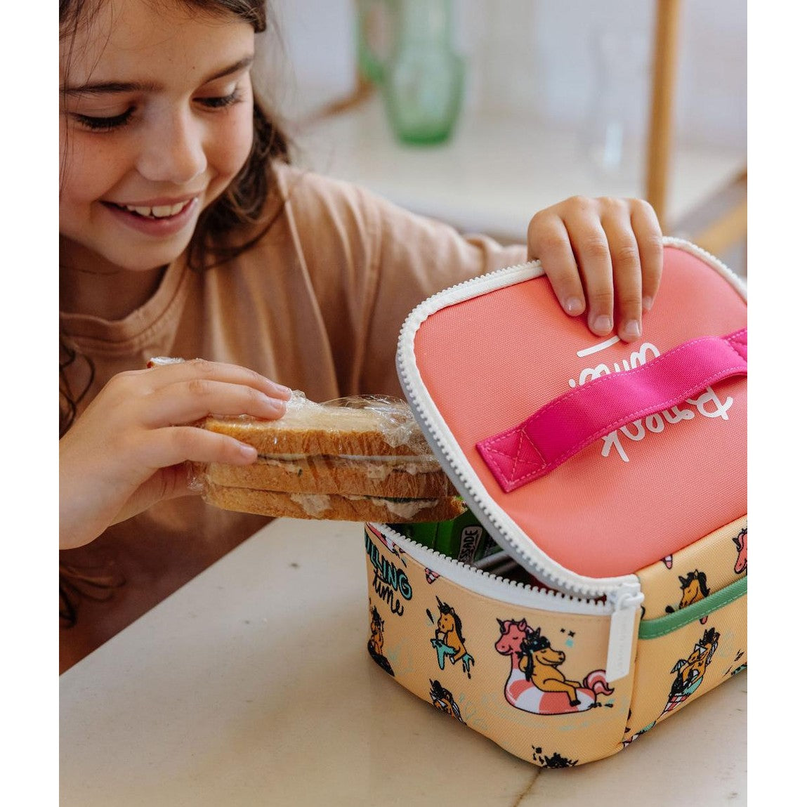 Smiling child opening beige unicorn lunch bag for snack time