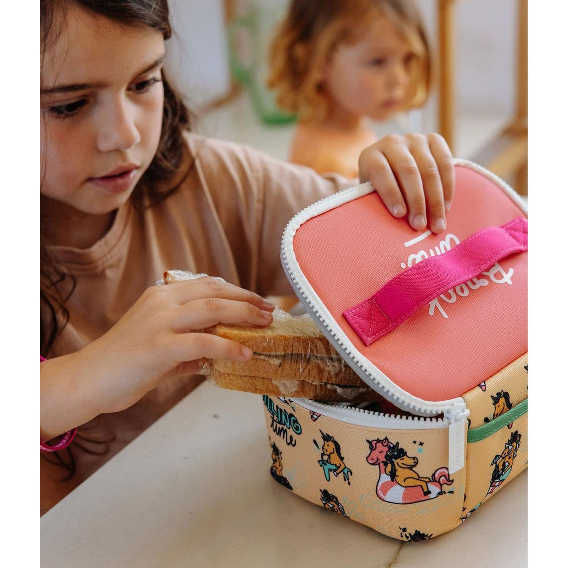 Girl inserting sandwich into colorful unicorn themed school lunch bag