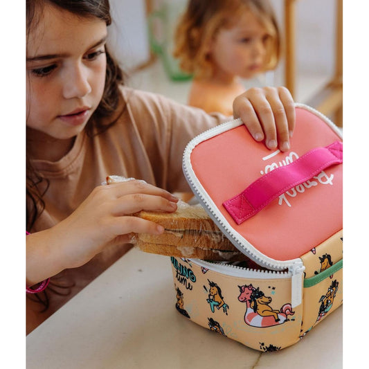 Girl inserting sandwich into colorful unicorn themed school lunch bag