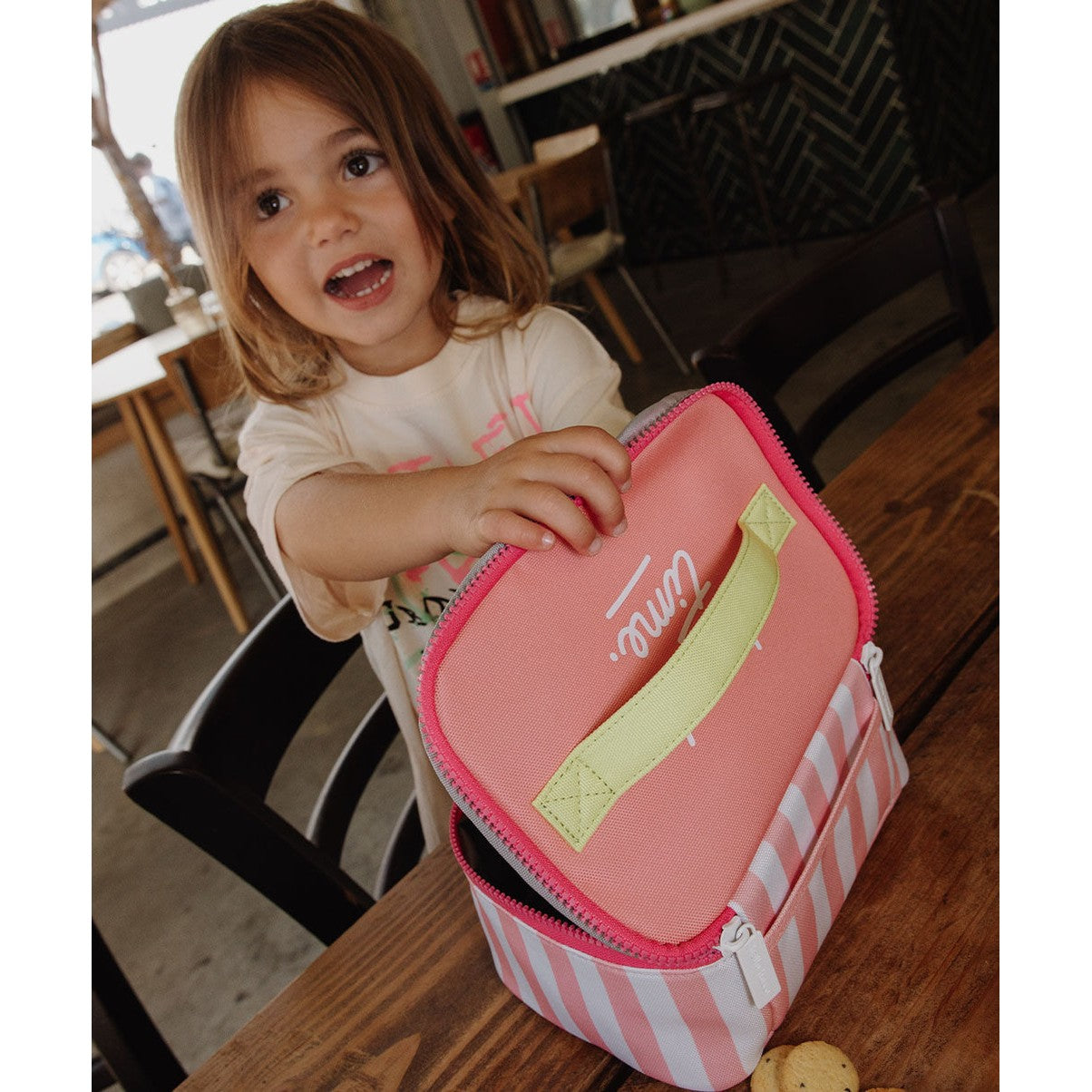 Girl holding open pink striped insulated lunch bag at table