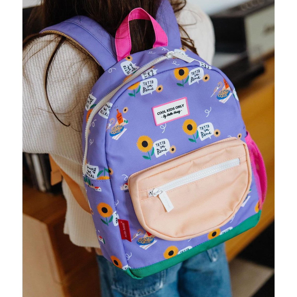 Child wearing purple Hello Hossy backpack featuring sunflower and food motifs on back