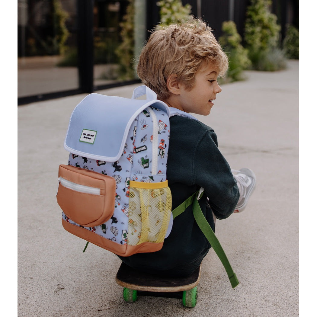 Child wearing light blue patterned backpack while riding a skateboard outdoors