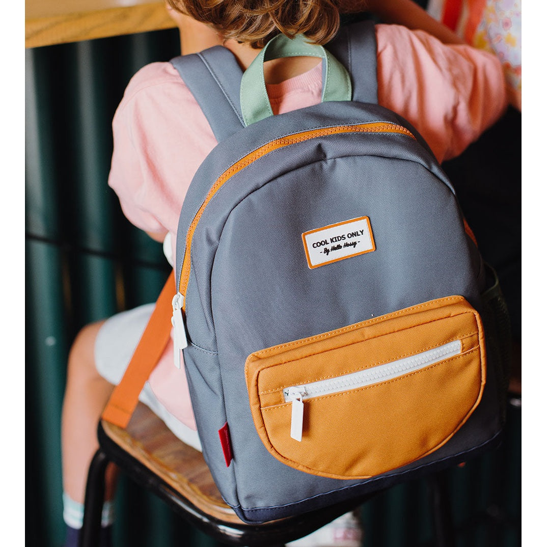 Child sitting with blue-gray backpack on back showing white COOL KIDS ONLY label