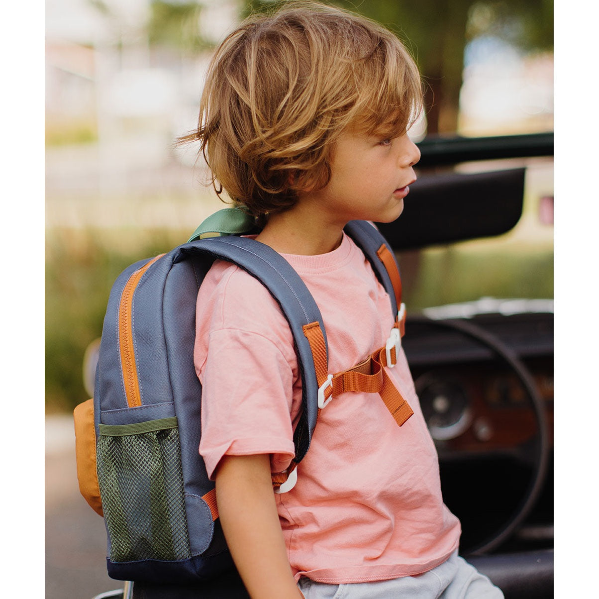 Child wearing blue-gray mini marine backpack with orange zipper and green mesh pocket