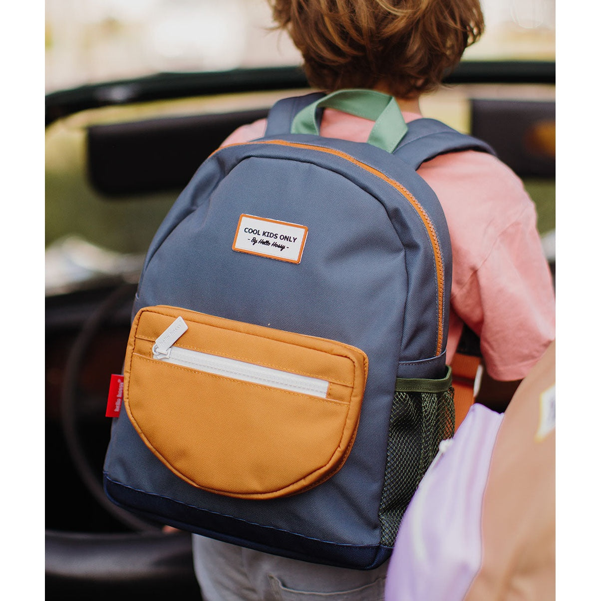 Kids standing with blue-gray backpack displaying green mesh pocket and orange details