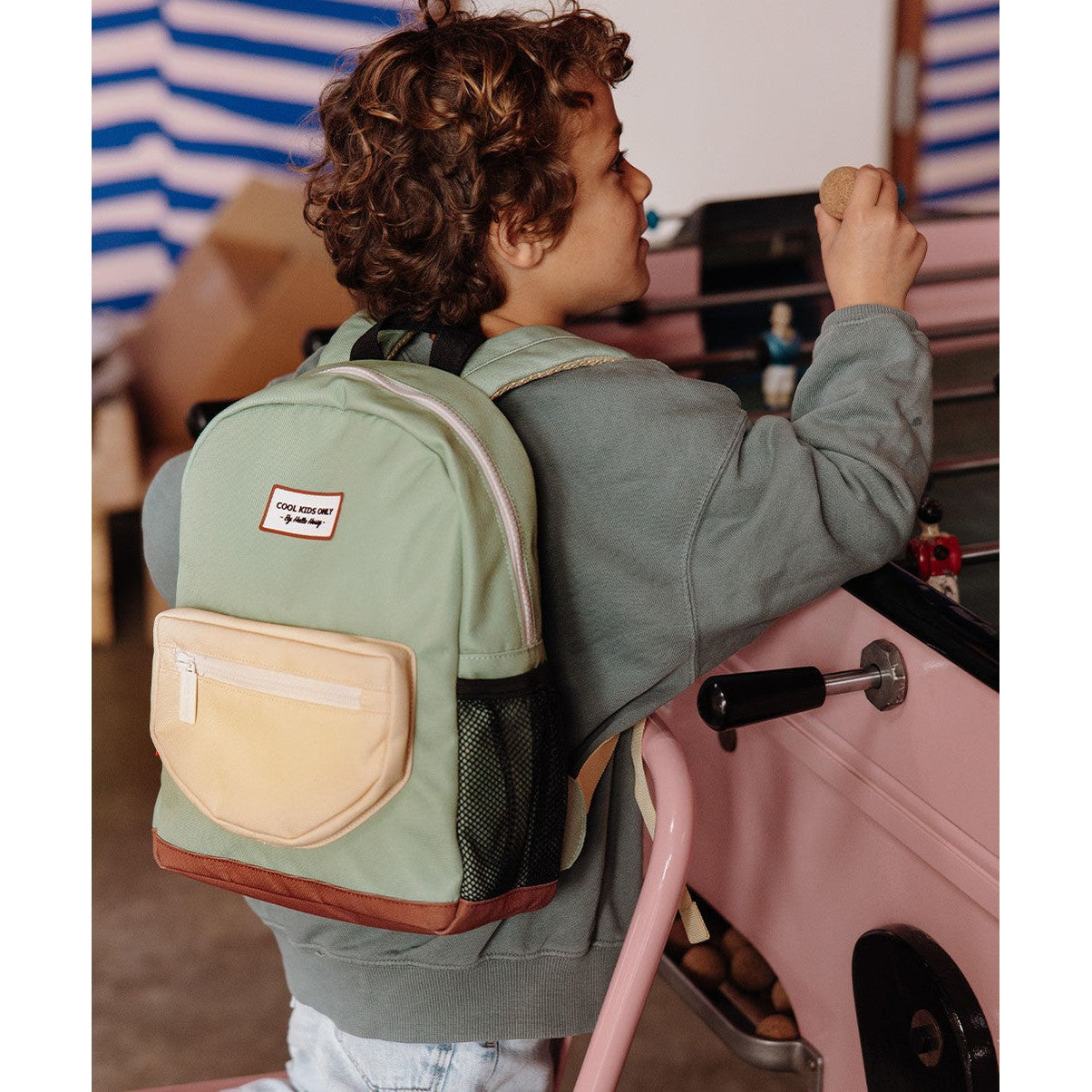 Child wearing light green Mini Pistache school backpack at foosball table