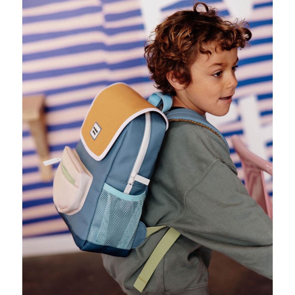 Side-back view of child in curly hair wearing blue kids school bag
