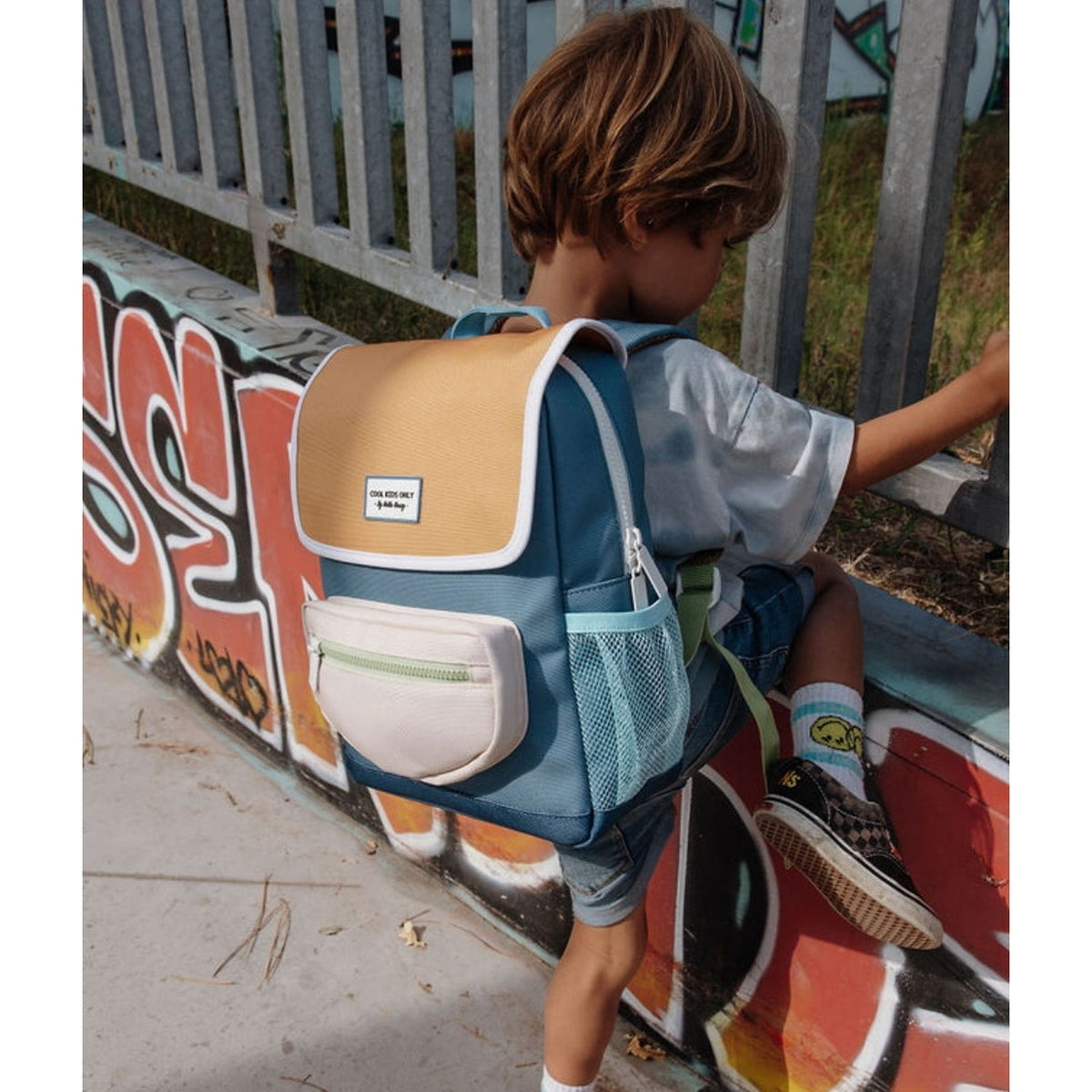Child sitting outdoors wearing blue and yellow eco-friendly mini backpack