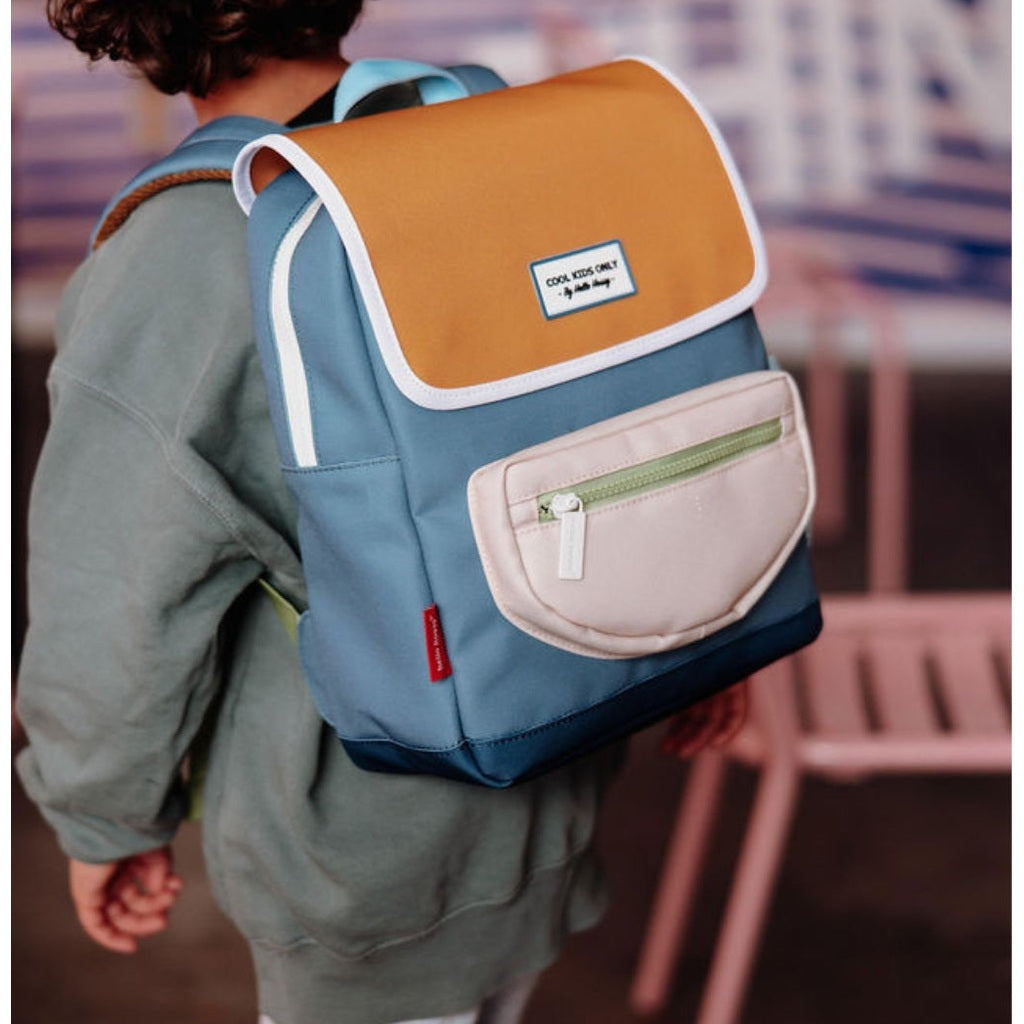 Child wearing blue Hello Hossy mini backpack with green zipper detail