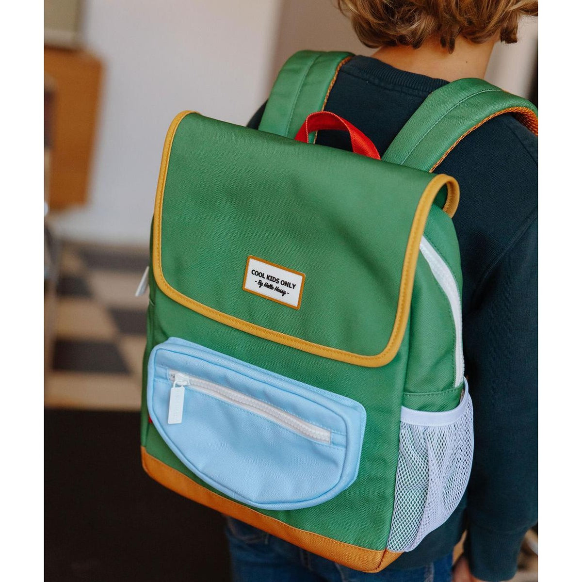 Back view of child wearing green square backpack with orange stitching straps