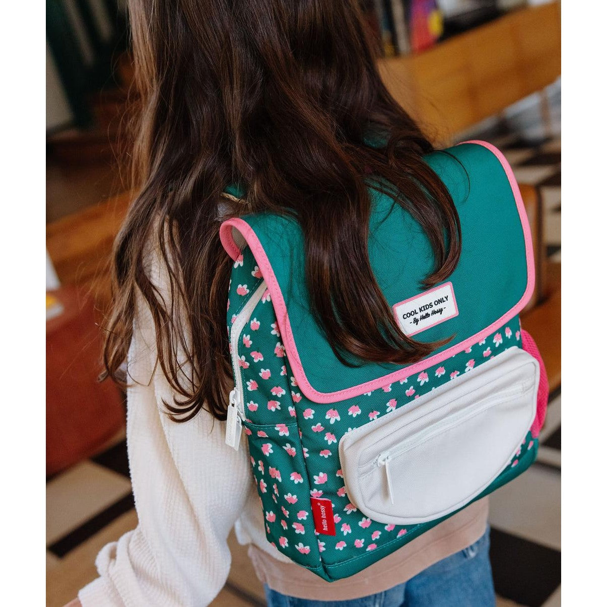 Backpack worn by child indoors showing green floral design and pink accents