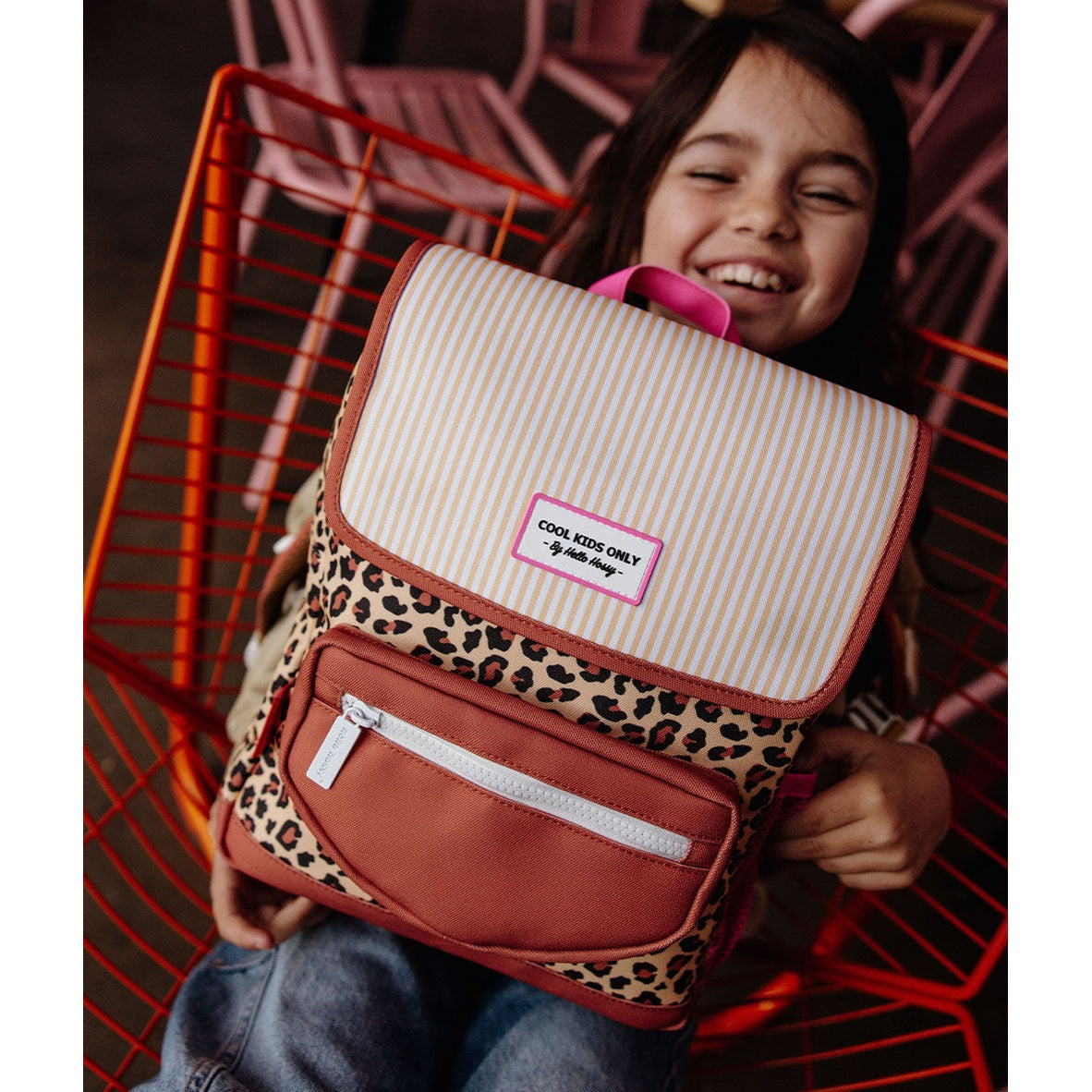 Girl holding Hello Hossy leopard print backpack in red wire basket