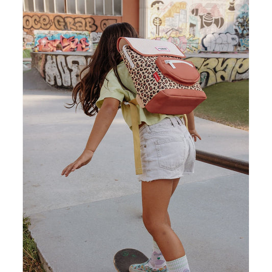 Child wearing beige leopard print backpack with pink accents at skatepark