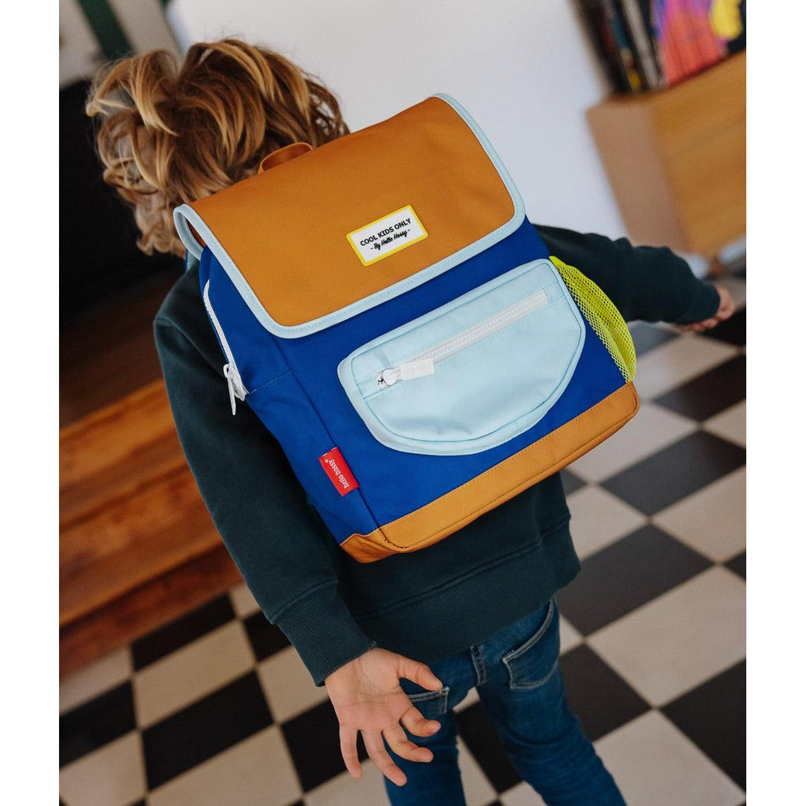Kid walking in checkered room wearing blue Hello Hossy bag