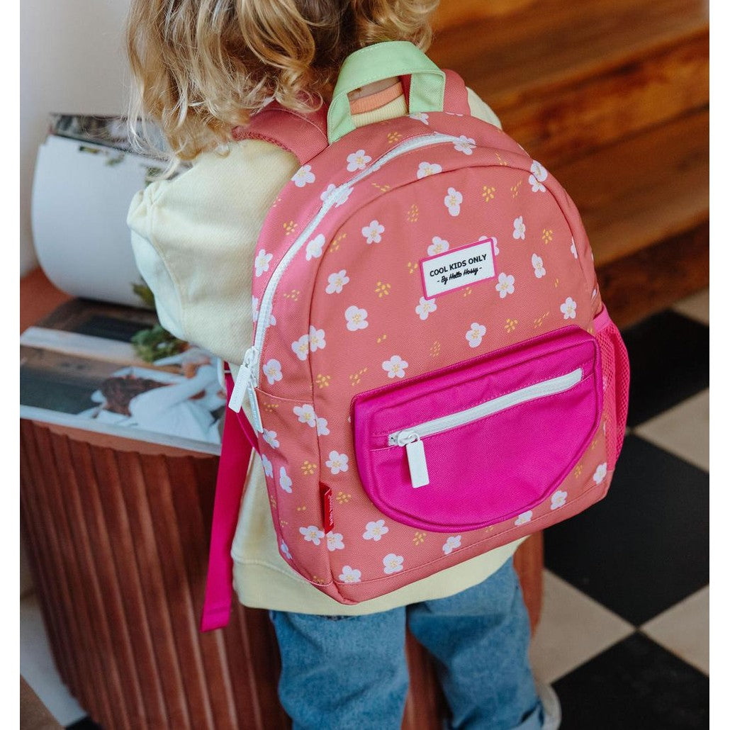 Child wearing peach-pink floral backpack standing on checkered floor