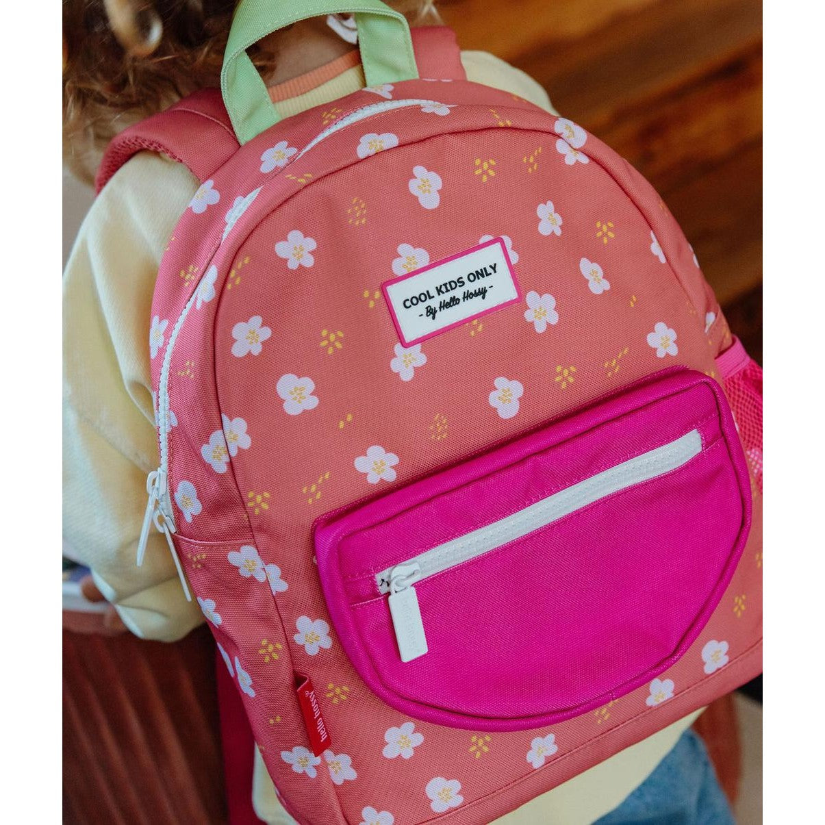 Child wearing coral pink floral backpack with front pocket and green handle