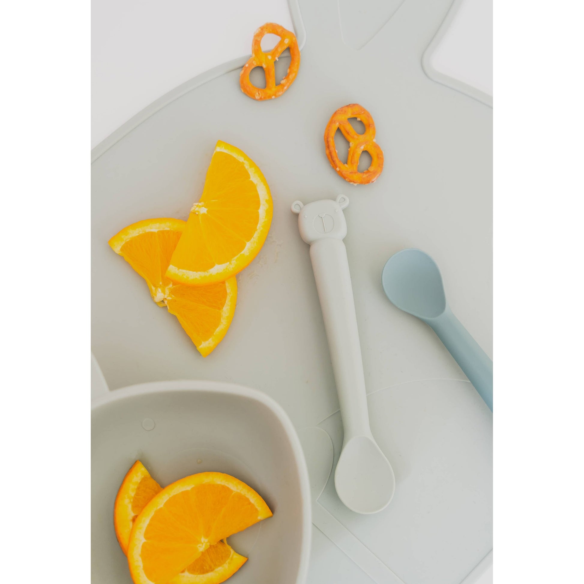 Gray Lili l'Ours silicone baby spoon on bear mat with fruit snacks