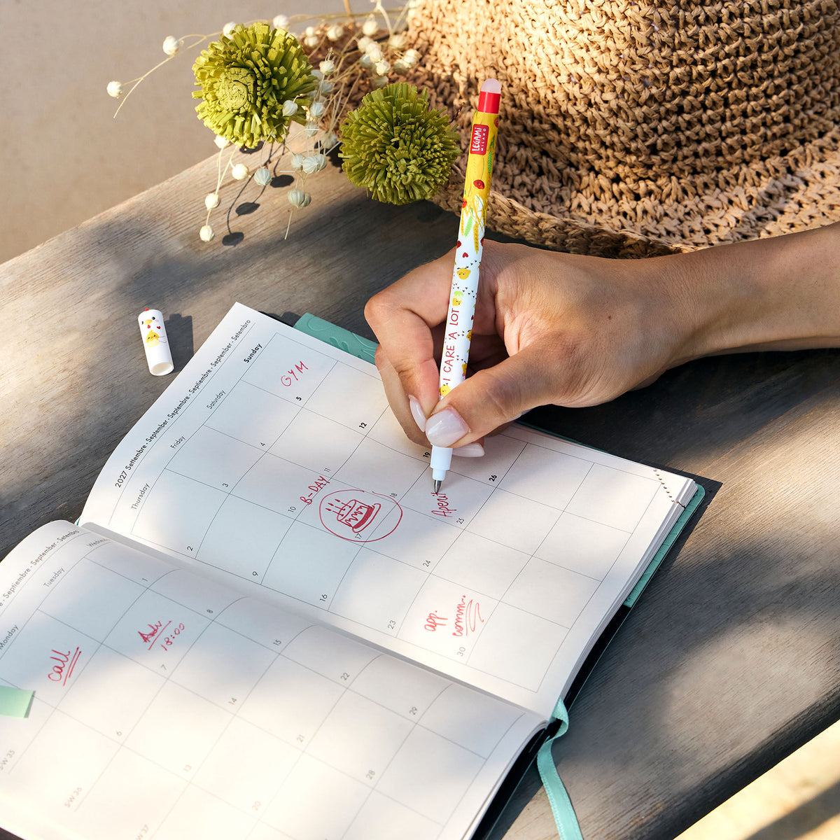 Hand using Legami erasable pen to write red ink entries in a September planner