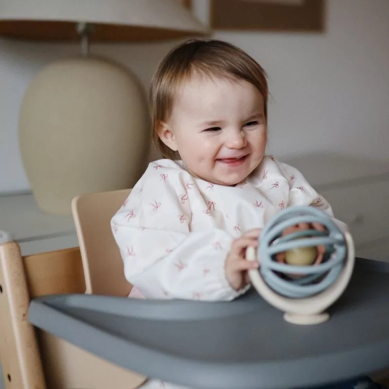 Baby holding La Mushie Suction Spinner Ball in high chair