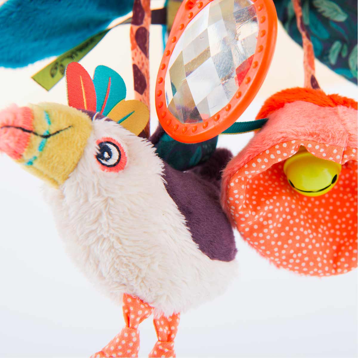 Close-up of toucan crest feathers and faceted orange oval mirror on baby toy