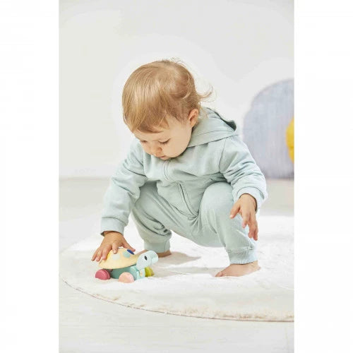 Toddler playing with Janod wooden pull-along turtle toy on white rug with light green hooded onesie