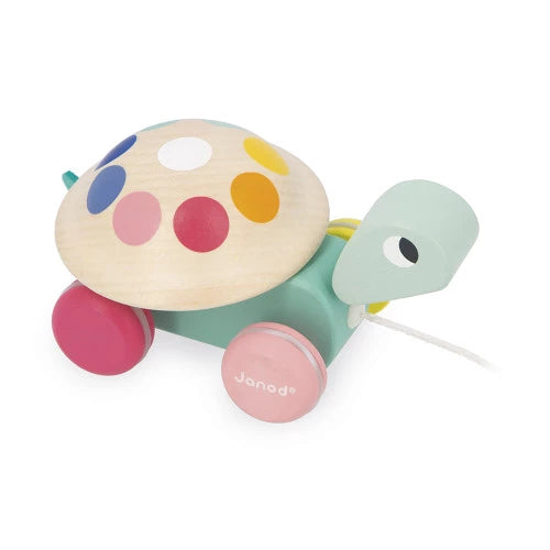 Close-up of Janod wooden turtle pull-toy featuring natural wood shell with colorful circular decals and pink wheel logo