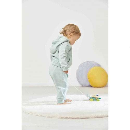 Child pulling Janod wooden turtle toy with white string across white rug near soft cushions