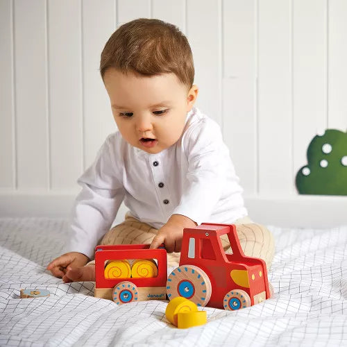 Toddler playing with Janod red wooden pull-along tractor and farm animal set