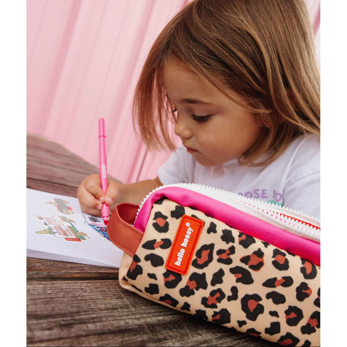 Girl writing at desk with Hello Hossy leopard print pencil case featuring pink zippers