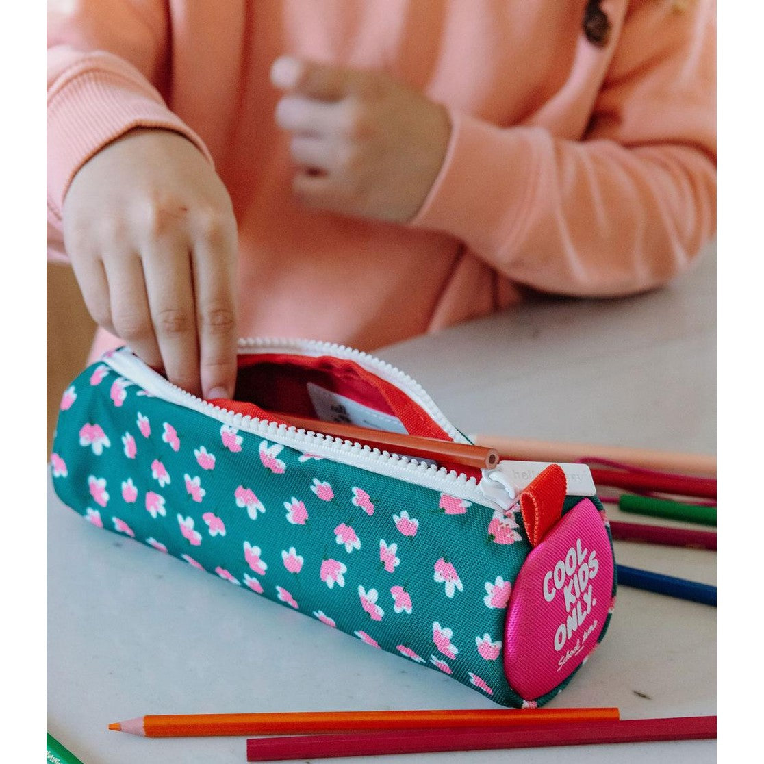 Child using green floral pencil case with orange pencils inside