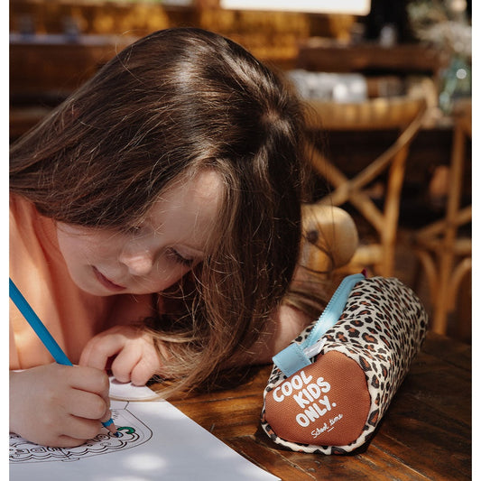 Girl drawing beside closed Hello Hossy leopard pencil case with COOL KIDS ONLY patch