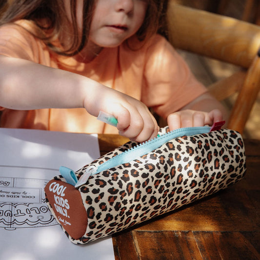 Child using Hello Hossy leopard pencil case at wooden desk with natural light