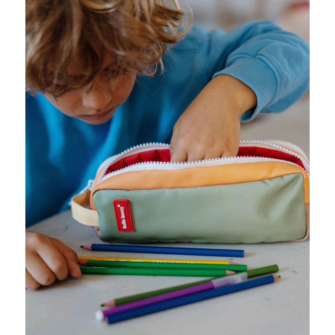 Child reaching into open Hello Hossy mini safari pencil case with colored pencils