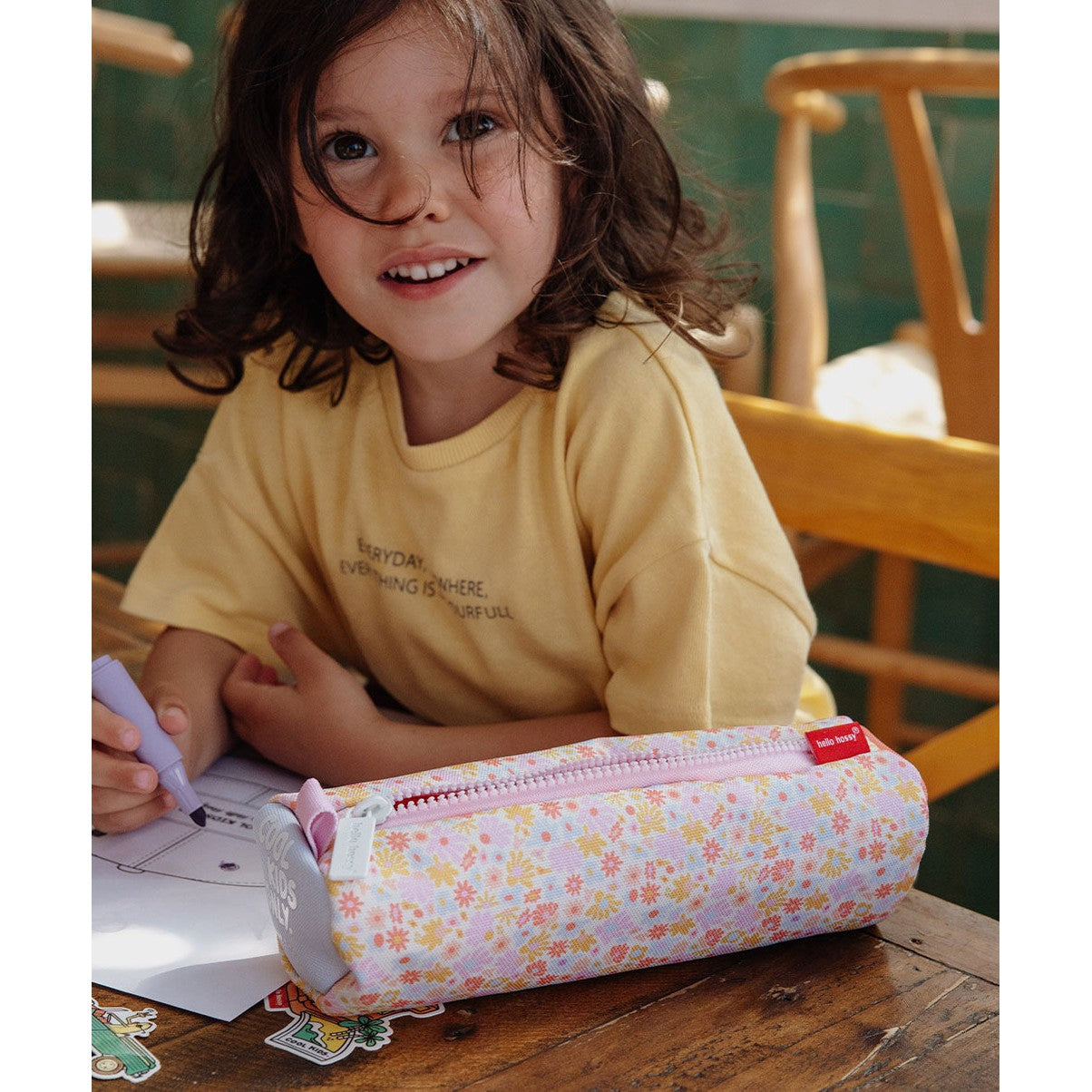 Girl holding marker next to pastel flower pattern cylindrical school pencil case