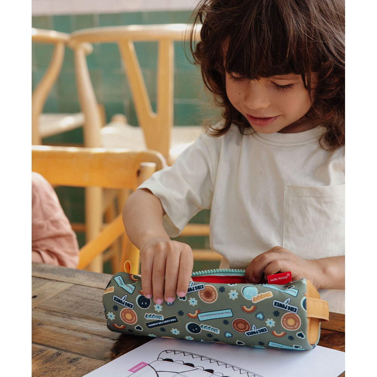 Child unzipping green smiley face pencil case on wooden table