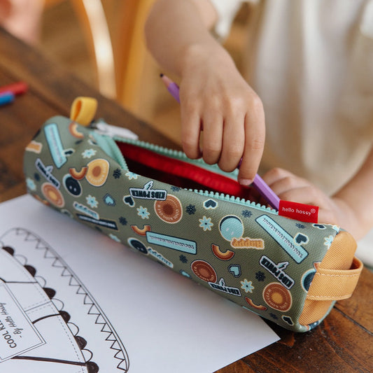 Child placing purple pencil into open green school pencil case