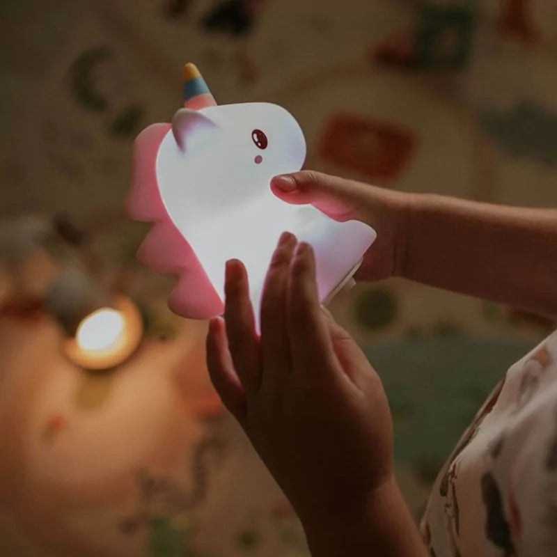 Child holding glowing LED unicorn night light in dim room