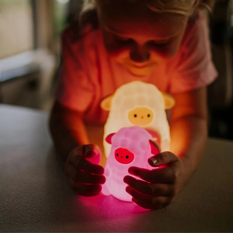 Child holding glowing pink and yellow sheep nightlights