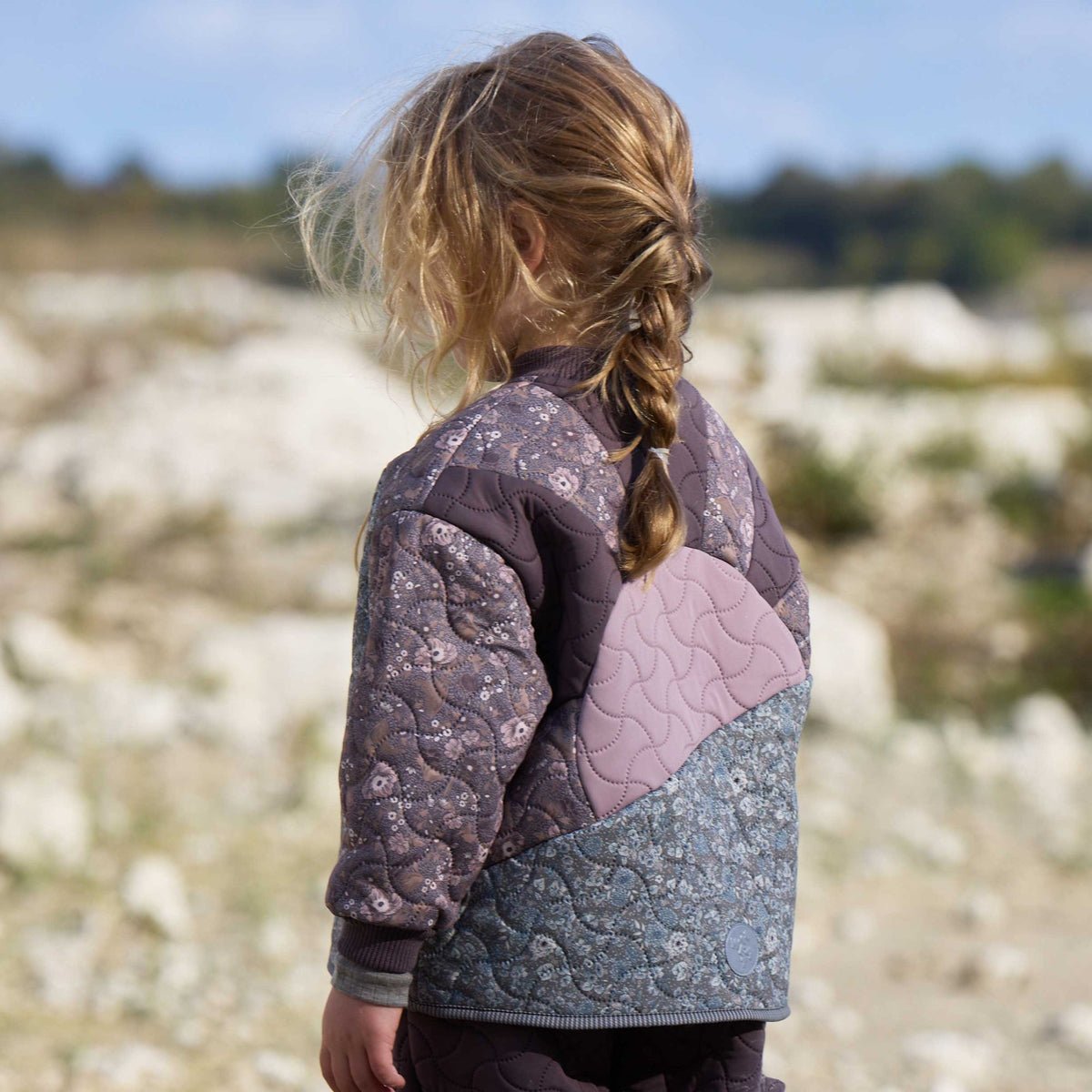 Child wearing Nanna patchwork quilted jacket outdoors in rocky landscape